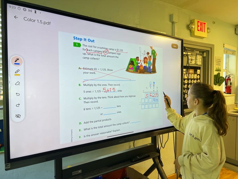 A student solving a math problem on the classroom smartboard
