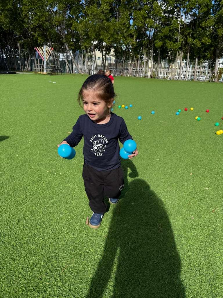A toddler running on the field with two balls