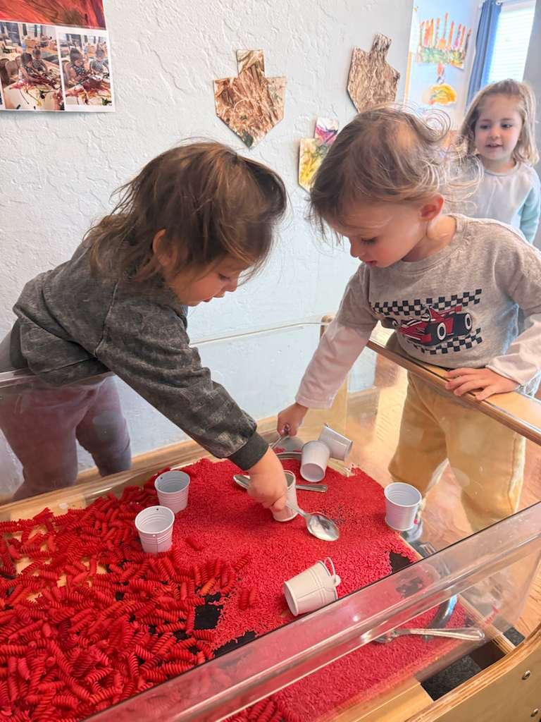 Children scooping at a red sensory bin