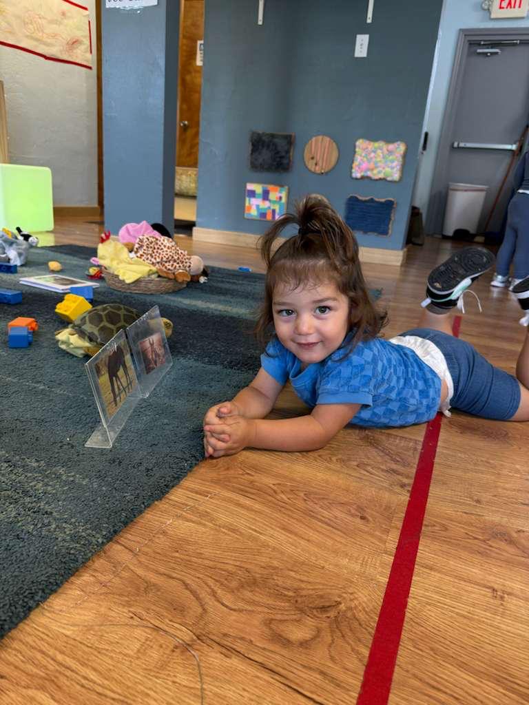 A smiling child lying on the classroom floor
